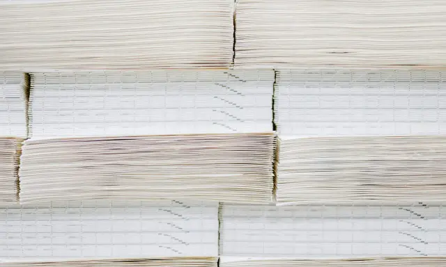 Grandes pilas de papel offset, algunas con finas líneas impresas, apiladas ordenadamente en un almacén.