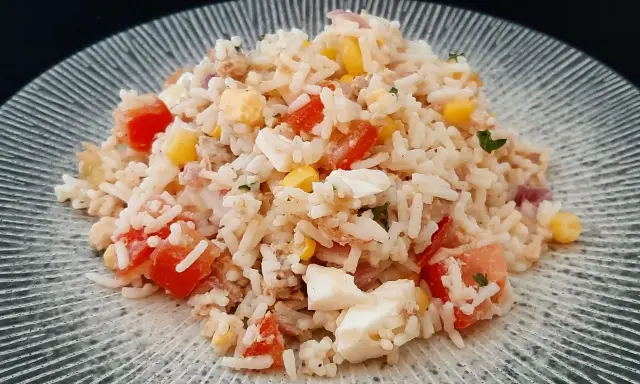 Salade de riz, thon, tomates, maïs et œuf dur sur une assiette grise.