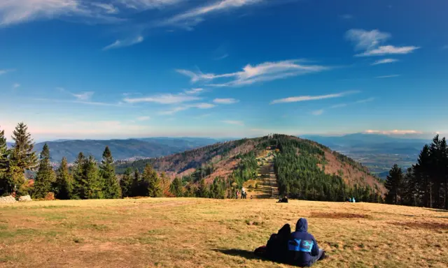 Widok na góry w Bielsku-Białej. Dwie osoby siedzą na trawie, podziwiając jesienny krajobraz i panoramę Beskidów.
