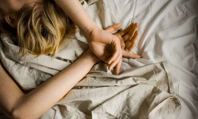 Blonde Haare auf einem Kissen, Arme schlafen nachts ein, Hände ruhen auf der Decke.