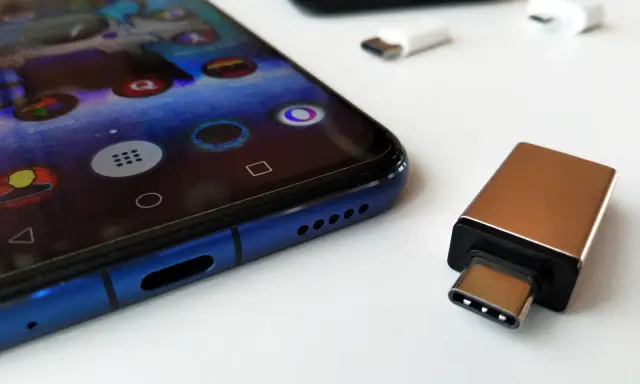 Złoty adapter USB-C i białe przejściówki leżą obok niebieskiego smartfona. Dowiedz się, jak podłączyć pendrive do telefonu.