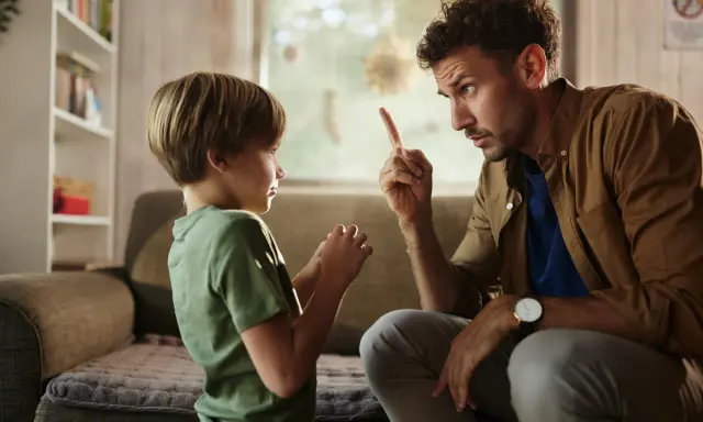 Un padre le dice no a su hijo, levantando el dedo índice en señal de advertencia. El niño escucha atentamente.