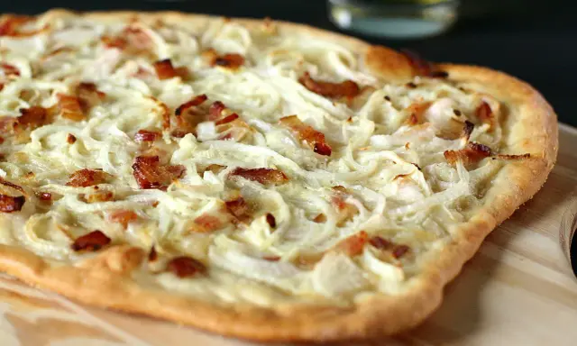 Flammekueche généreuse garnie d'oignons crus ou cuits et de lardons croustillants, prête à être dégustée.