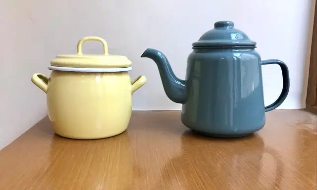En gul gryta och en blå kaffepanna i emalj, liknande en klassisk kockums kaffepanna, står på ett träbord.