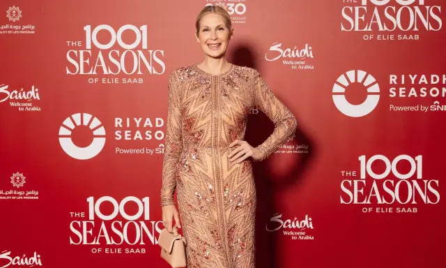 A woman in a sparkling celio saab gown poses at an event with "1001 Seasons of Elie Saab" branding.