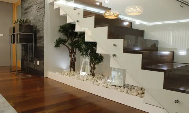 Elegante subida de escalera interior con plantas decorativas y piedras blancas.
