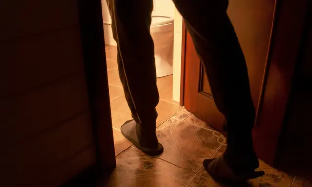 Nocne wstawanie do toalety, częste sikanie w nocy. Widok na nogi w kapciach i drzwi łazienki.