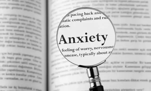 Lupa powiększa definicję "Anxiety" w książce, opisując uczucie niepokoju, które może prowadzić do fobi.