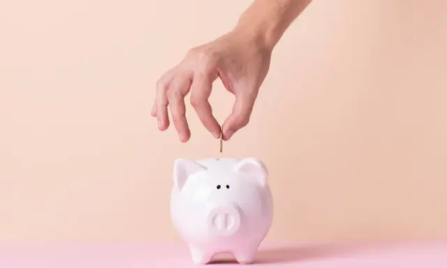 Mano inserta moneda en alcancía blanca, simbolizando cómo empezar una cuenta de ahorro.