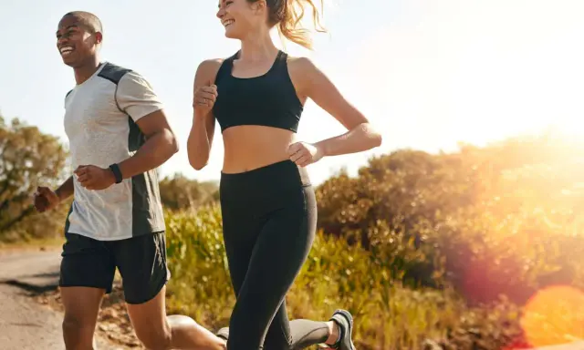 Ein Mann und eine Frau joggen lachend auf einem Feldweg. Die Sonne scheint, und die Atmung beim Joggen ist gleichmäßig und tief.
