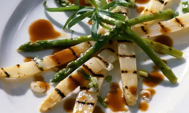 Gegrillter Spargel auf einem Teller, mit einer würzigen Sauce beträufelt und garniert mit frischen Kräutern.