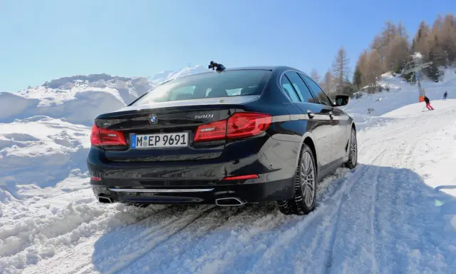 Schwarzer BMW 540i G30 fährt durch tiefen Schnee auf einer Skipiste, bergauf mit Skilift im Hintergrund.
