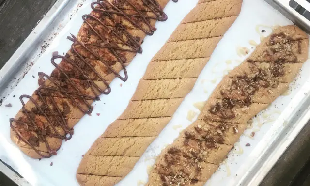 Tre långa, avlånga kakor på en plåt. En är dekorerad med chokladglasyr och hackad choklad, en annan med strössel och en tredje med honung och nötter. Perfekt för ett kolakakor recept!