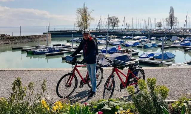 Mann mit Rennrad am Bodensee, bereit für die Bodensee Umrundung. Boote im Hafen.