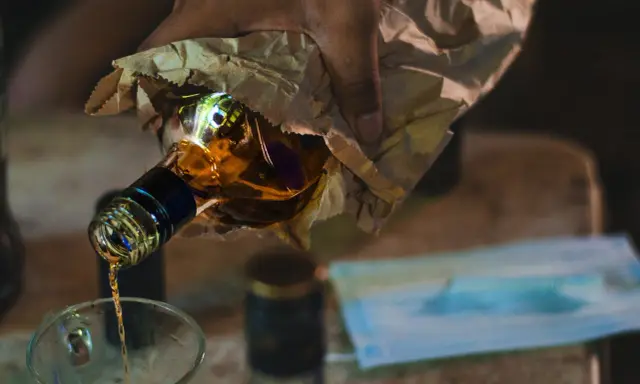 Ręka trzyma butelkę z alkoholem, z której nalewany jest płyn do szklanki. To może być początek drogi do dawki śmiertelnej alkoholu.