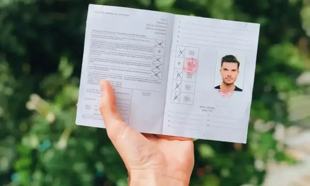Osoba trzyma dokument z pieczątkami i zdjęciem, wyglądający jak międzynarodowe prawo jazdy.