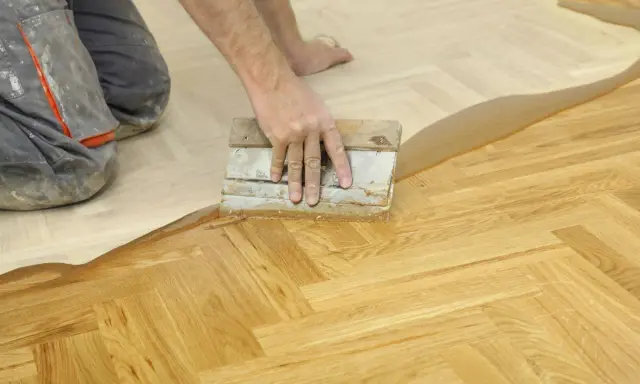 Un artisan applique un produit sur un parquet en chevrons. Une étape essentielle pour la réparation parquet.