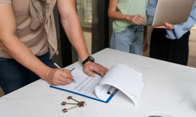 Firma de un contrato de alquiler, quizás un modelo 111 para que sirva de acuerdo. Llaves y portátil presentes.