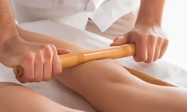 Relaksacyjny masaż pałeczkami bambusowymi na nogach. Terapeuta wykonuje głęboki masaż, przynoszący ulgę i odprężenie.