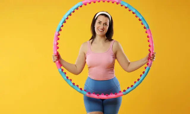 Uśmiechnięta kobieta z hula hop. Dowiedz się, jak dobrać hula hop do wzrostu, by ćwiczenia były efektywne i przyjemne.