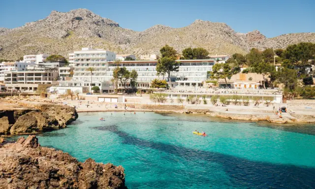 Majorka, gdzie najlepiej? Widok na turkusową zatokę z hotelami i plażą w tle, góry w oddali. Idealne miejsce na wakacje.