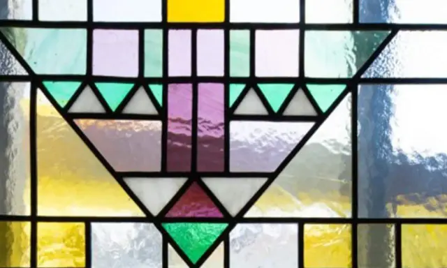 Un motif géométrique coloré orne cette fenêtre vitraux, mêlant le jaune vif, le violet doux et le vert émeraude.