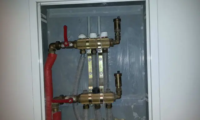 Widoczny zawór RTL na powrocie systemu ogrzewania podłogowego. Metalowa obudowa skrywa skomplikowaną instalację hydrauliczną.