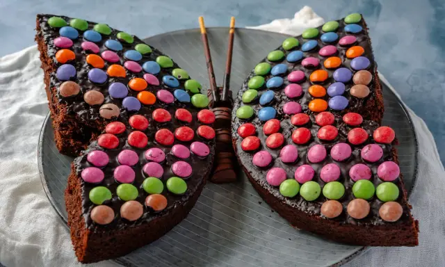 Ein schokoladiger Smarties Kuchen in Form eines Schmetterlings, der mit bunten Smarties dekoriert ist.