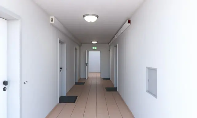 Ein langer, heller Flur mit mehreren Türen und einem grünen Notausgangsschild. Dieser notwendiger Flur ist gut beleuchtet und wirkt einladend.