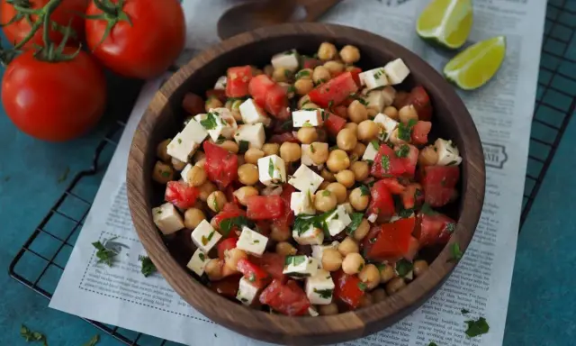Ein köstlicher, **high protein salat** aus Kichererbsen, Tomaten und Feta in einer Holzschale, garniert mit Petersilie.