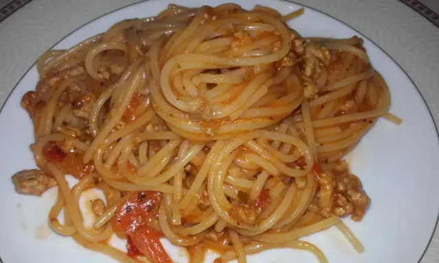 Pyszne spaghetti bolognese z passaty, z mielonym mięsem i kawałkami pomidorów, podane na białym talerzu.