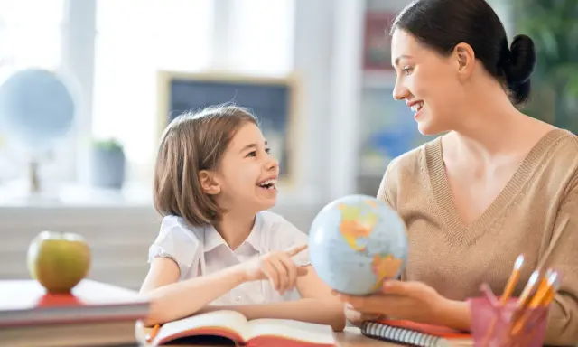 Niña y maestra sonríen mientras exploran un globo terráqueo. Un ejemplo de como ser un buen profesor, inspirando curiosidad y aprendizaje.