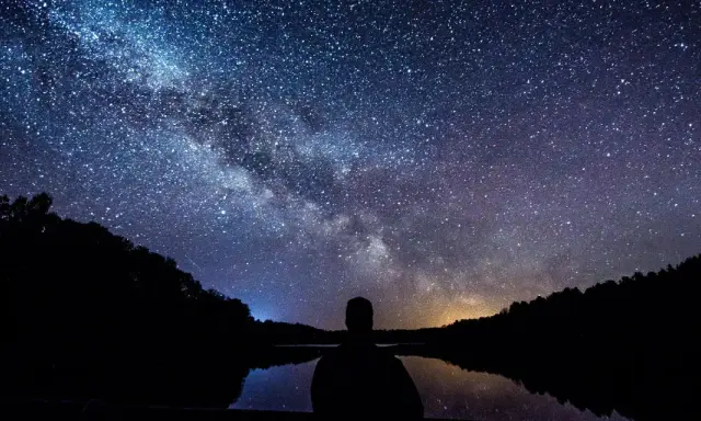 Zachwycająca fotografia astronomiczna Drogi Mlecznej nad jeziorem. Sylwetka człowieka kontempluje kosmos.