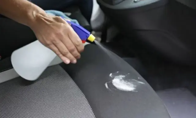 Mano rocía un asiento de coche con un limpiador para eliminar manchas de flujo.