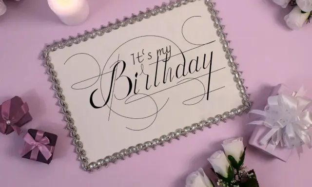Eleganckie zaproszenie na urodziny w stylu savoir vivre. Biała kartka z ozdobnym napisem "It's my Birthday", otoczona prezentami i świecą.