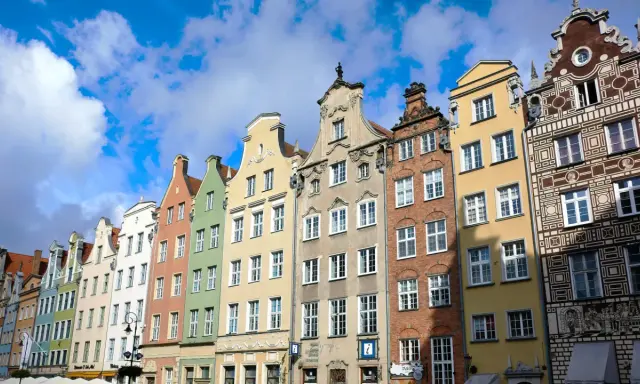 Kolorowe kamienice w Gdańsku, w trakcie remontu elewacji, prezentują się malowniczo na tle błękitnego nieba z chmurami.