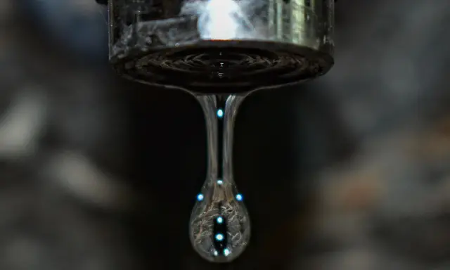 Un grifo que gotea, con una gota de agua capturada en el aire, reflejando luces como pequeñas estrellas.