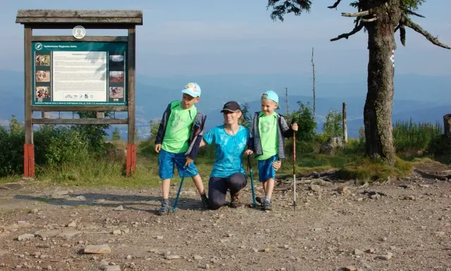 Rodzina na szczycie Baraniej Góry. Dzieci z kijkami trekkingowymi, mama klęczy obok.