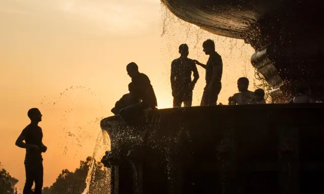 Silhouette fotografia di persone che si rinfrescano in una fontana al tramonto, con l'acqua che scintilla contro il cielo arancione.