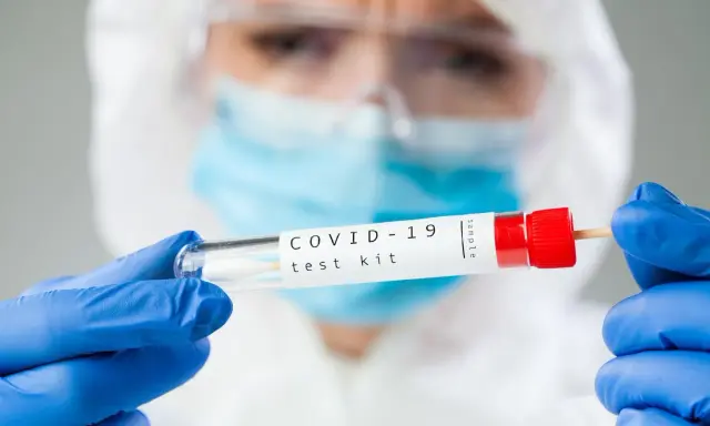 Osoba w kombinezonie i rękawiczkach trzyma probówkę z wymazem. Zastanawiasz się, ile kosztuje test na covid?