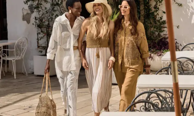 Tre donne passeggiano con stile, mostrando come vestirsi al mare con abiti leggeri e accessori estivi.