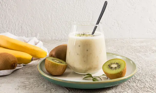 Un verre de smoothie banane kiwi, garni de graines de chia, avec des fruits frais autour.