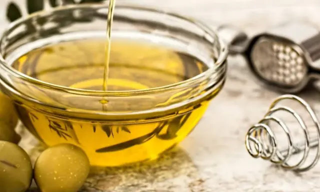 Aceite de oliva vertiéndose en un bol de cristal, rodeado de aceitunas. Varios tipos de aceite comestible para cocinar.