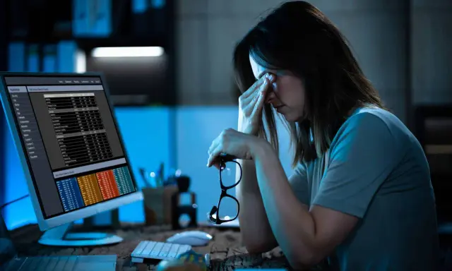 Femme fatiguée devant un écran, lunettes à la main. La hyperconnectivité définition se reflète dans son regard las face aux données.
