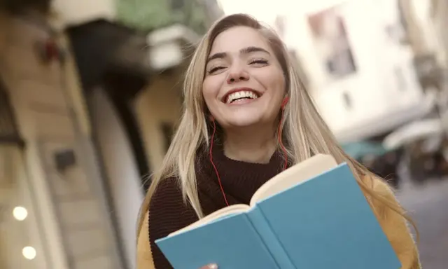 Uśmiechnięta dziewczyna z książką i słuchawkami na ulicy. Może to być studentka, która właśnie skończyła lekcje w szkole w Danii.