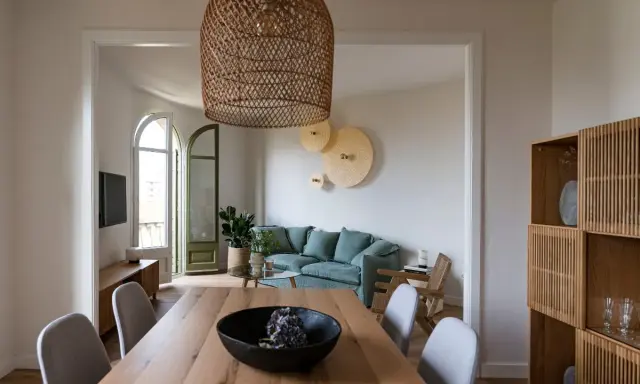 Comedor y sala minimalista para espacios pequeños. Mesa de madera, sillas grises, sofá verde menta y estantería de roble.