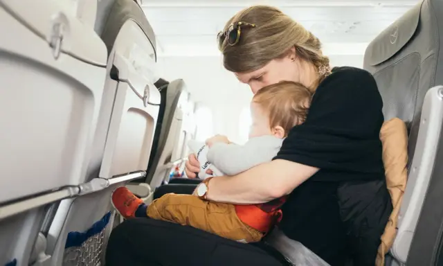 Mama tuli do samolotu z dzieckiem. Siedzą obok siebie, a dziecko bawi się zabawką.