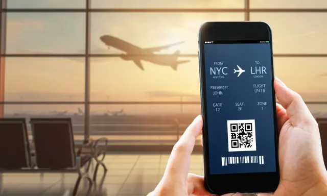 Bilet lotniczy na telefonie: lot z NYC do LHR, pasażer John, bramka 12. IATA co to? To kod lotniska.