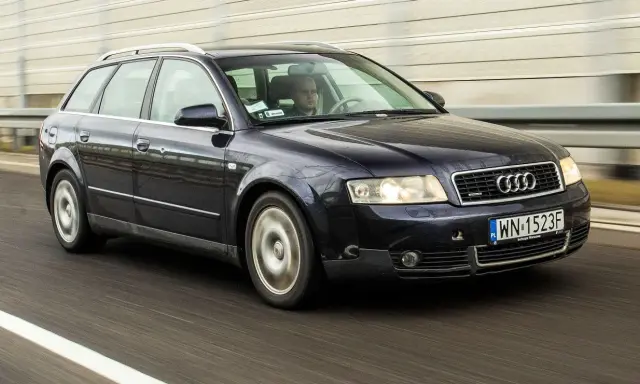 Ciemnogranatowe Audi A4 B6 2.0 Avant pędzi autostradą. Kierowca skupiony na drodze.