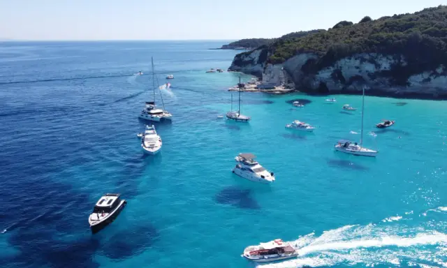 Båtar i turkost vatten vid en klippig kust, en idyllisk vy från Paxos, Grekland.